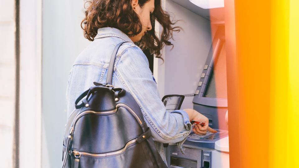 Woman using credit card withdrawing money from an ATM machine outside a branch of savings bank.