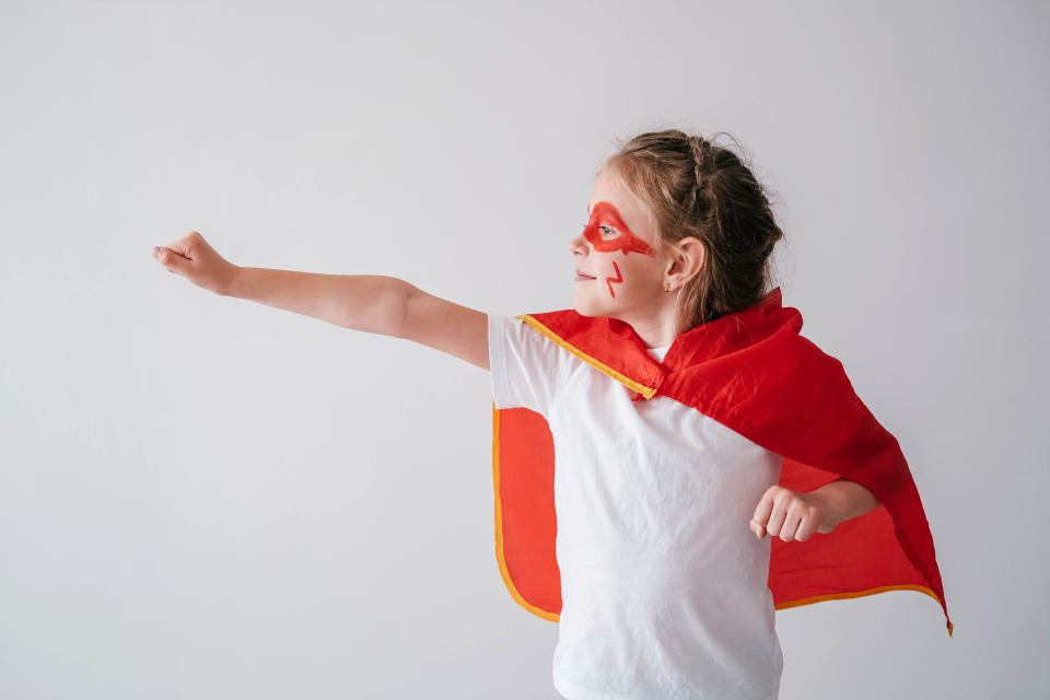 A young girl dressed as a superhero with a red cape