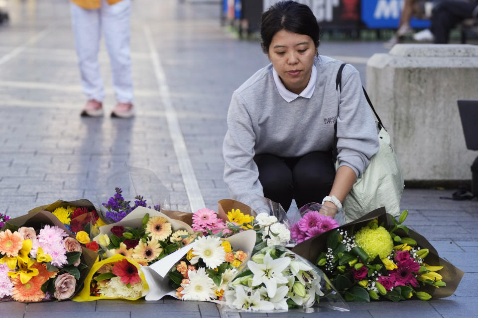 A woman brings flowers to an impromptu memorial at Bondi Junction in Sydney, Sunday, April 14, 2024, after several people were stabbed to death at a shopping center a day earlier. Police have identified Joel Cauchi, 40, as the assailant that stabbed six people to death at a busy Sydney shopping center Saturday before he was fatally shot by a police officer. (AP Photo/Rick Rycroft)