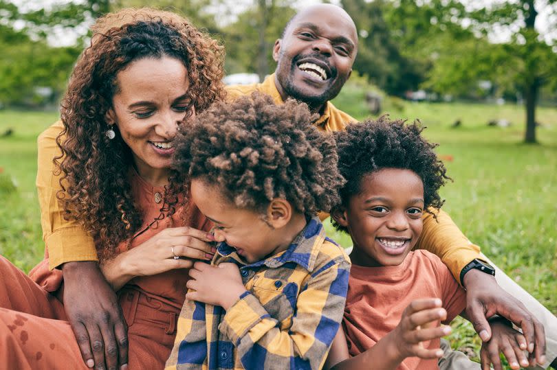 Happy family, parents and children in a park in summer, smile and relax on grass field for quality time, love and nature. Happiness, picnic and portrait of people outdoor and playing together