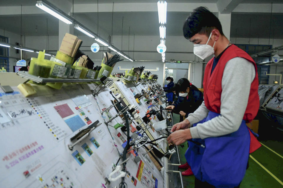 In this Feb. 13, 2020, photo, masked workers assembly wiring for automobile at a factory in Qingdao in east China's Shandong province. Automakers are gradually reopening factories in China that were idled by anti-virus controls as they try to reverse a sales slump in their biggest market. (Chinatopix via AP)