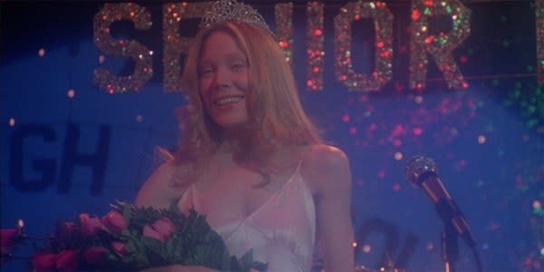 Carrie standing on stage with the homecoming crown on her head during the senior prom