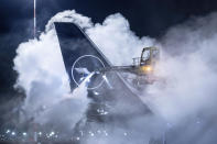 A Lufthansa aircraft is de-iced at Frankfurt Airport, Germany, early Wednesday, Jan. 17, 2024. Heavy snowfalls and freezing rain across Germany Wednesday led to the cancellation of hundreds of flights and trains, crashes on icy roads, and school closures. (Boris Roessler/dpa via AP)