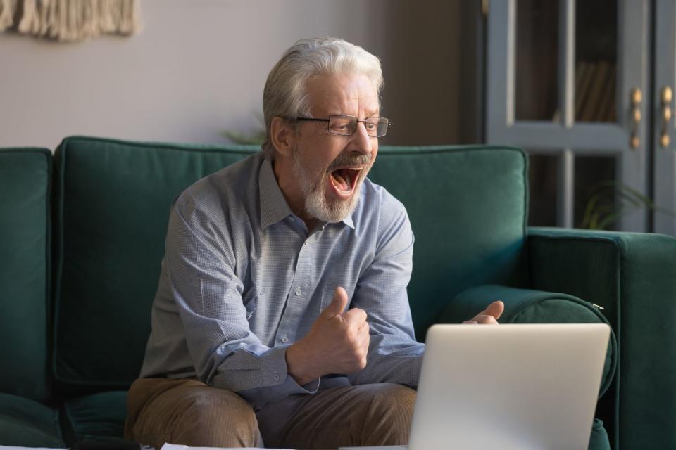 Man celebrates on couch while looking at laptop computer