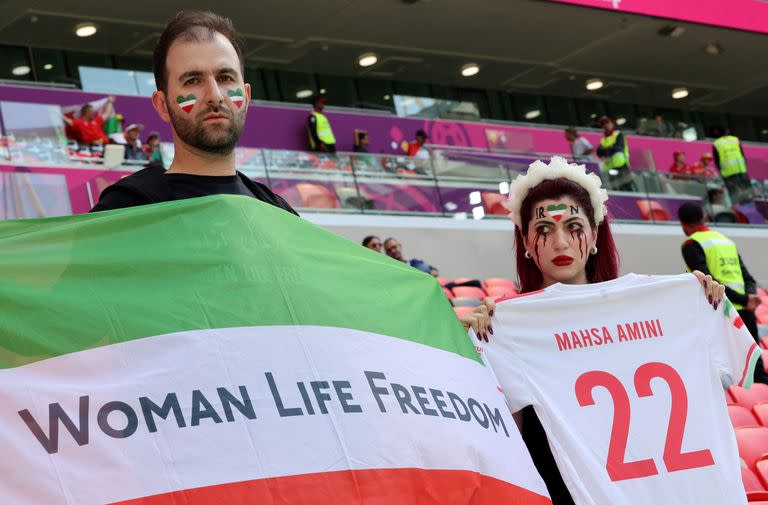 An Iran's supporter with blood tears make up on her face holds a football jersey reading the name of Mahsa Amini, the 22-year-old Iranian Kurdish woman who died at the hospital after been arrested by the morality police for violating Iran's strict dress code, poses with another supporter holding a flag reading "Woman life freedom" as they attend the Qatar 2022 World Cup Group B football match between Wales and Iran at the Ahmad Bin Ali Stadium in Al-Rayyan, west of Doha on November 25, 2022. - Iran has been rocked by more than seven weeks of nationwide protests over the death of 22-year-old Kurdish Iranian woman Masha Amini while in the custody of the Tehran morality police. (Photo by Giuseppe CACACE / AFP)