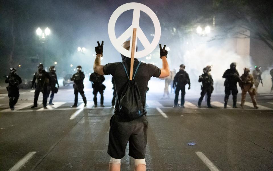 A protester holds up two peace signs in front of a wall of Department for Homeland Security officers and local police in Portland, Oregon - Mark McKenna