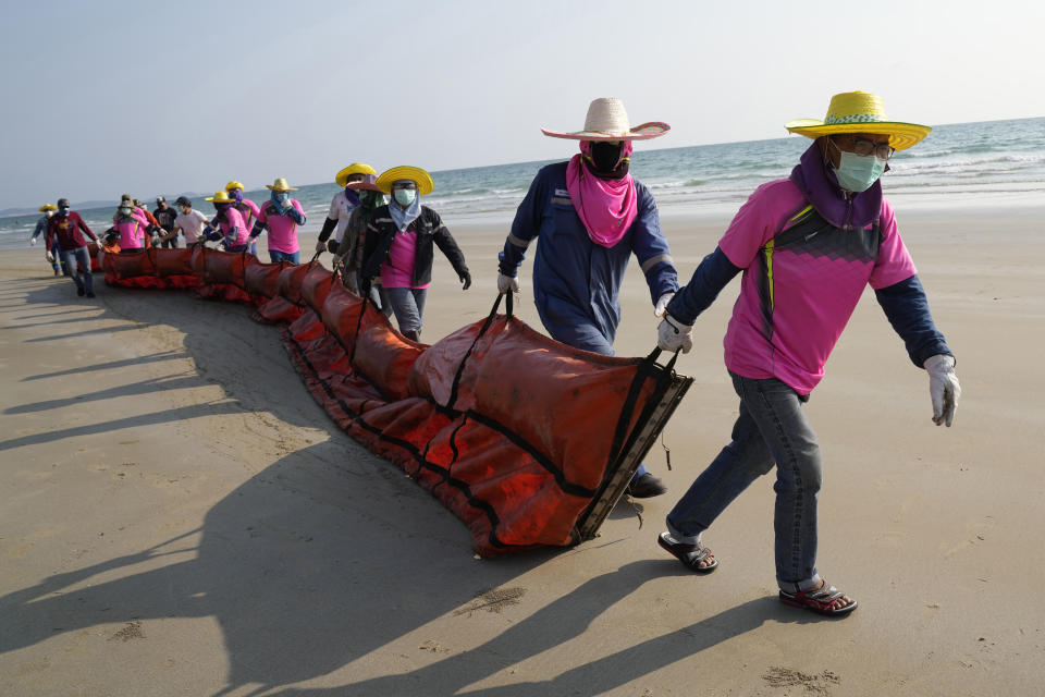 Workers drag an oil spill boom out onto Mae Ram Phueng Beach in hopes of containing any oil washing ashore from a recent spill off the coast of Rayong, eastern Thailand, Friday, Jan. 28, 2022. An oil slick off the coast of Thailand continued to expand Friday and was approaching beaches on the east coast, home to fragile coral and seagrass, officials said. (AP Photo/Sakchai Lalit)