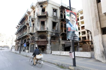 A man rides a bicycle past a poster depicting Syria's President Bashar al-Assad near the new clock square in the old city of Homs, Syria December 7, 2015. REUTERS/Omar Sanadiki