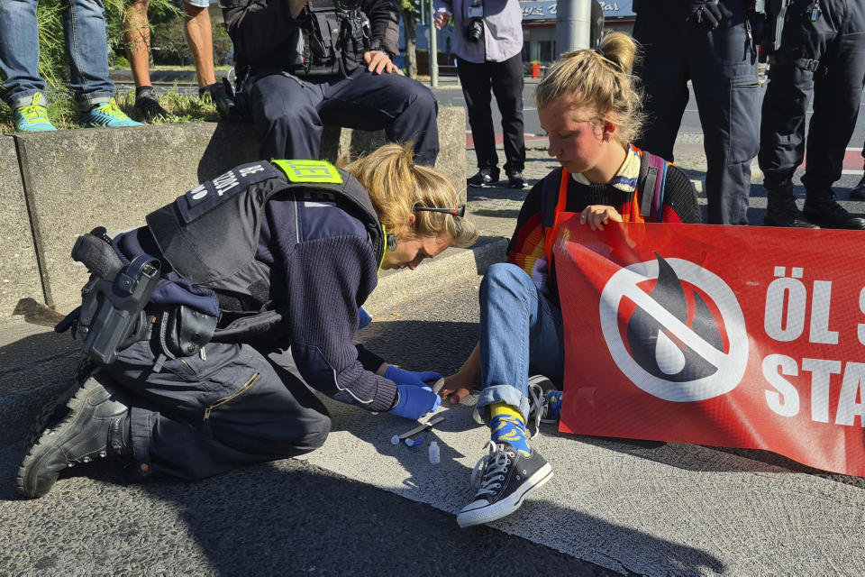 A police officer uses cooking oil to loosen the hand of a protester with the group Uprising of the Last Generation who glued herself to a road in Berlin in protest against the government's climate policy on Monday, July 11, 2022. The group claims the world has only a few years left to turn the wheel around and avoid catastrophic levels of global warming. (AP Photo/Frank Jordans)