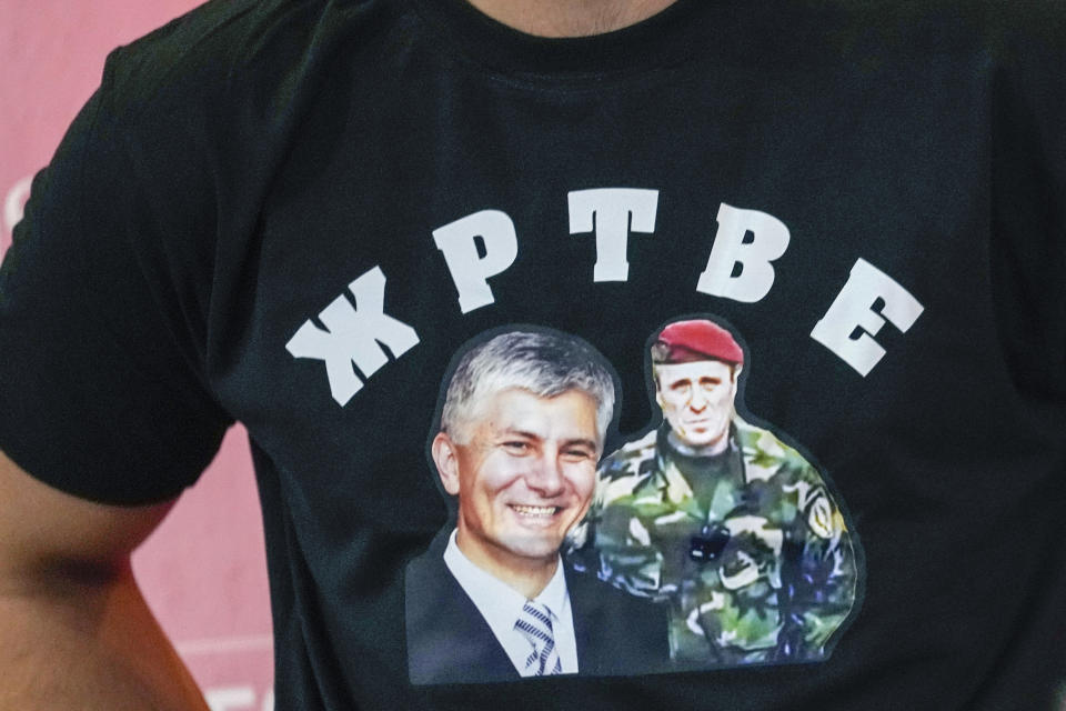 FILE - A man walks wearing a shirt showing Serbia's slain prime minister Zoran Djindjic, left, and Zvezdan Jovanovic, former deputy commander of the elite secret service "Red Berets", was convicted for the assassination of Djindjic, reading: "Victims", in Belgrade, Serbia, on Oct. 22, 2021. In 2003, two years after he orchestrated Milosevic's extradition to the U.N. war crimes tribunal in The Hague, Netherlands in 2001, Djindjic was gunned down by a special paramilitary unit that used to fight in Bosnia and Croatia. (AP Photo/Darko Vojinovic, File)