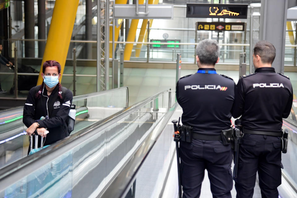 A passenger wearing a face mask as a protective measure looks at two police officers as they use a travelator at the Madrid-Barajas Adolfo Suarez Airport in Barajas on March 20, 2020. - The coronavirus toll in Spain rose to 1,002 today following the deaths of 235 people in the past 24 hours, the health ministry said. The number of cases also soared to 19,980, after another 2,833 infections were confirmed over the same period, the ministry's emergencies coordinator said. (Photo by JAVIER SORIANO / AFP) (Photo by JAVIER SORIANO/AFP via Getty Images)