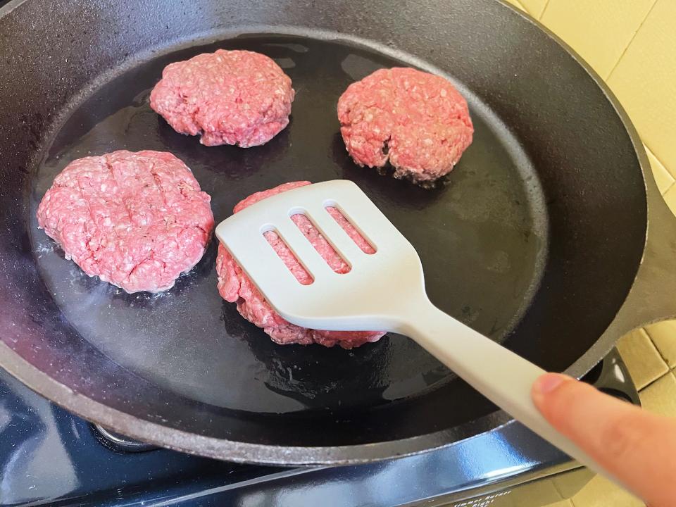 burger patties in a cast iron skillet with a spatula