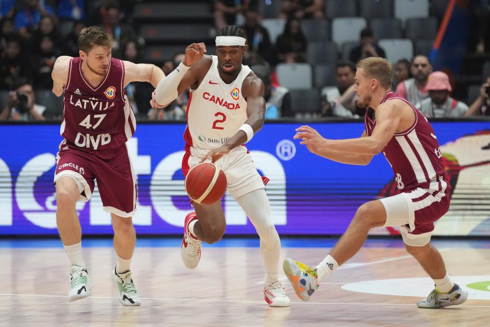 Canada guard Shai Gilgeous-Alexander (2) dribbles the ball against Latvia guard Arturs Kurucs (47) and guard Arturs Zagars (55) during the Basketball World Cup group H match between Canada and Latvia at the Indonesia Arena stadium in Jakarta, Indonesia, Tuesday, Aug. 29, 2023. (AP Photo/Tatan Syuflana)