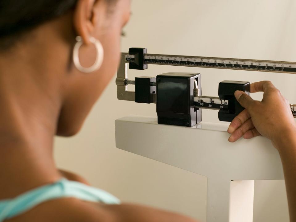 a side view from the shoulders up of a woman weighing herself on a scale