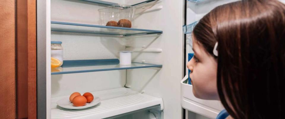 Worried girl looking at the almost empty fridge due to a crisis