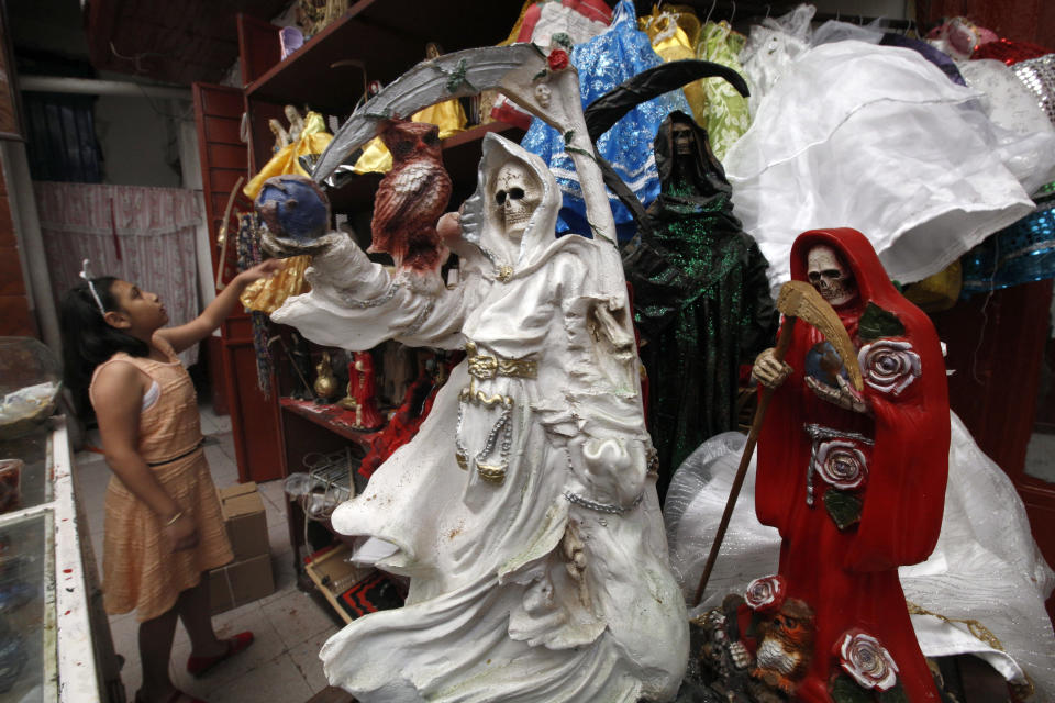 FILE - In this Feb. 19, 2017 file photo, a child arranges statues of La Santa Muerte, or "Our Lady of Holy Death," on the edge of Mexico City's Tepito neighborhood. A New Mexico archbishop is renewing his call for Catholics to stop worshipping the skeleton folk saint, saying he fears some mistakenly believe the Grim Reaper-like figure is a Roman Catholic Church-sanctioned saint. Santa Fe Archbishop John Wester recently told The Associated Press he believes some Catholics may be fooled into venerating Santa Muerte even though the focus on death runs counter to the church's teachings. (AP Photo/Marco Ugarte, File)