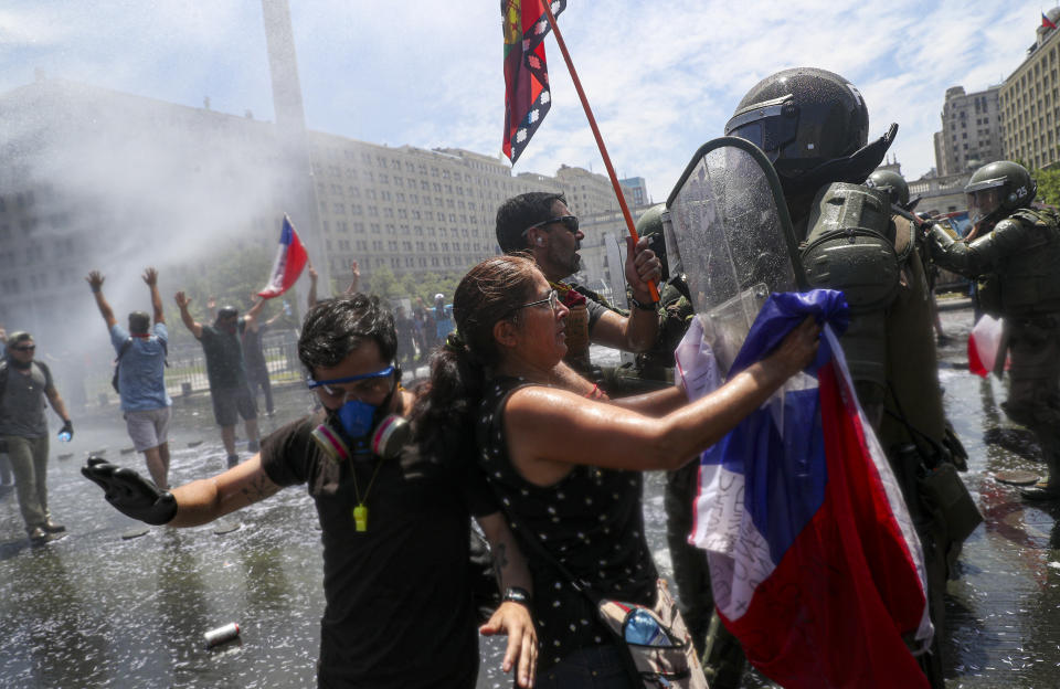 A woman places a Chilean flag on the riot shield of a Chilean police officer during a protest march in front to La Moneda presidential palace in Santiago, Chile, Tuesday, Nov. 12, 2019. Students in Chile began protesting nearly a month ago over a subway fare hike. The demonstrations have morphed into a massive protest movement demanding improvements in basic services and benefits, including pensions, health, and education. (AP Photo/Esteban Felix)