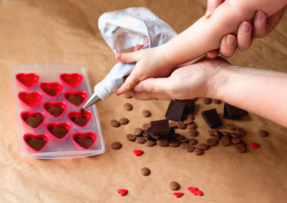 Kid learning how to cook in a cooking class together with mother. Mommy and me Handmade valentines day dessert. Family Making chocolate candy, Hands filling heart shaped mold from pastry bag