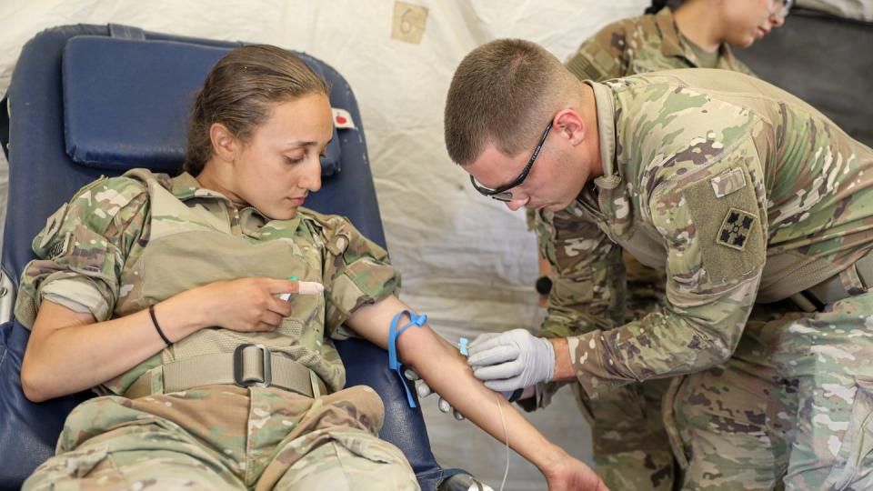 Spc. Hayden Hutto, a medic assigned to Charlie Medical Company, 64th Brigade Support Battalion, 3rd Armored Brigade Combat Team, 4th Infantry Division, inserts a needle into U.S. Army Sgt. Kiana Lassalle, a medic also assigned to Charlie Medical Company, during a walking blood bank training at Skwierzyna, Poland, Aug. 10, 2022. (Sgt. Tara Fajardo Arteaga/Army)