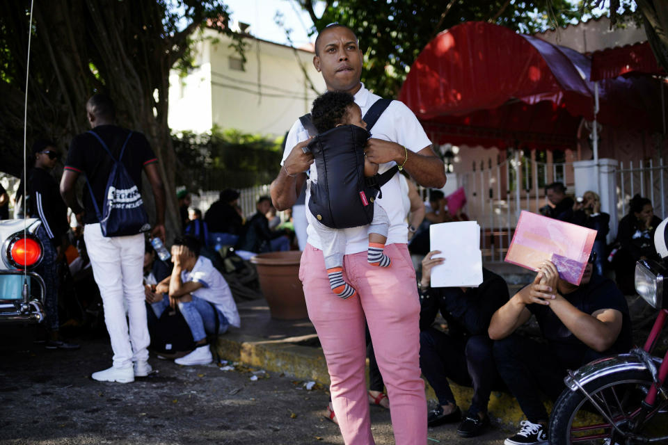 In this April 26, 2019, photo, a man holds his baby while he waits his turn to enter Nicaragua's embassy to apply for travel visas for him and his son to Nicaragua, in Havana, Cuba. The surge over the past several months has been propelled in part by loosened traveled restrictions in Central America and deteriorating living conditions in Cuba. (AP Photo/Ramon Espinosa)