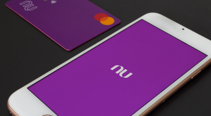 Nubank mobile app on white cell phone and credit card on black surface. NU stock.