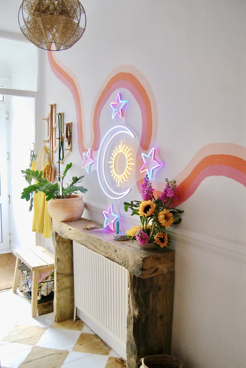 Entryway with credenza/sideboard with flowers, plants. Colorful neon and mural os wavy stripes on the wall