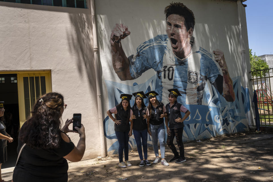 Students graduating from the General Las Heras elementary school, where Lionel Messi also attended school, pose for a group photo wearing their graduation hats by a mural of Messi, on the last day of school in Rosario, Argentina, Wednesday, Dec. 14, 2022. (AP Photo/Rodrigo Abd)