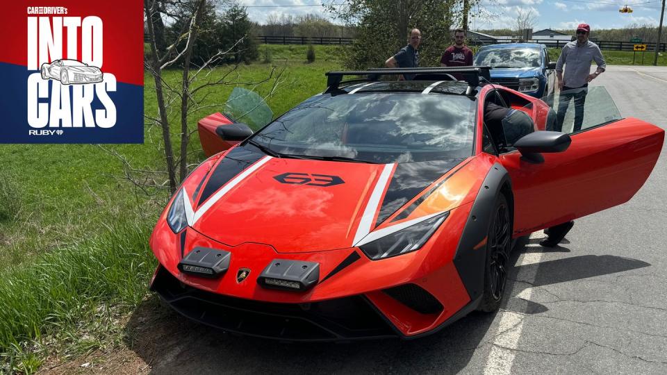 a red sports car with a spoiler parked on a road with people standing around