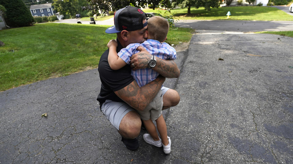 Mike Gilpatrick, who as a teenager was incarcerated at the Youth Development Center, embraces his son, who just completed his first day of school, outside their home, Wednesday, Sept. 8, 2021, in Nashua, N.H. Gilpatrick, 38, filed a lawsuit Monday Sept. 13, alleging he was physically and sexually abused at the former YDC in Manchester, which has been the target of a criminal investigation since 2019 and is slated to close in 2023. (AP Photo/Charles Krupa)