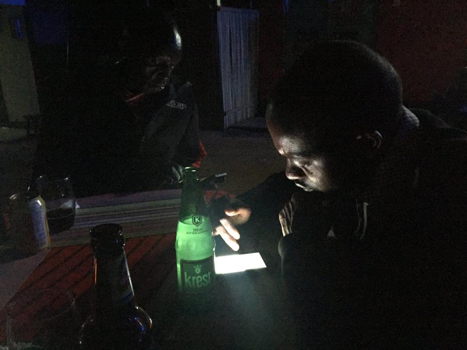 In a darkened room, phone screens light two men's faces.