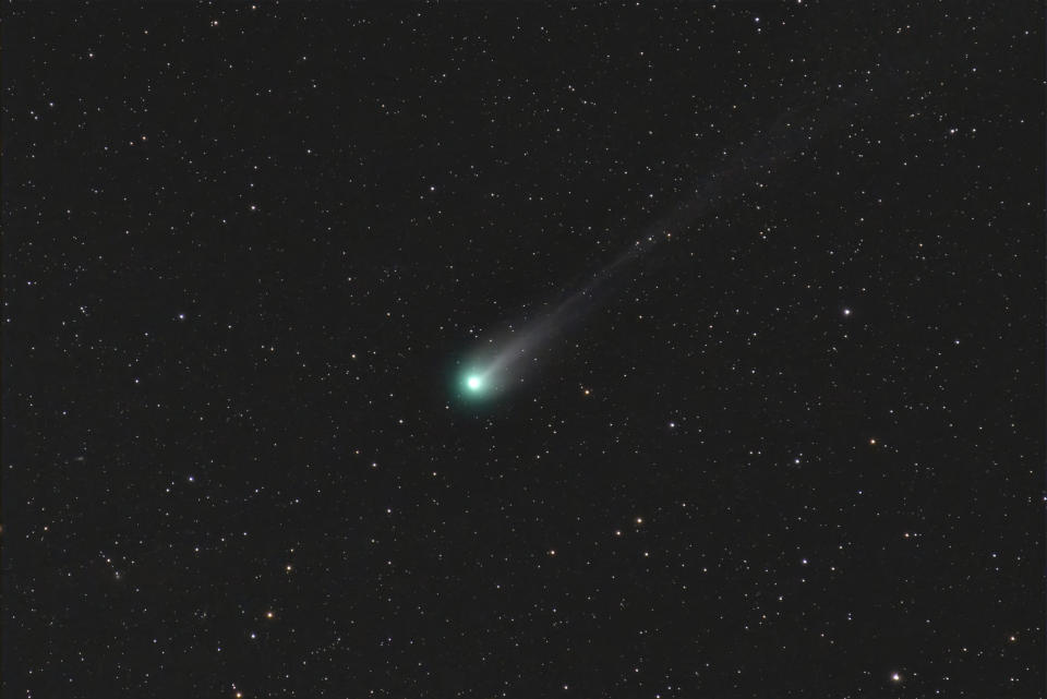 comet glowing green and white with a long tail against a backdrop of stars.