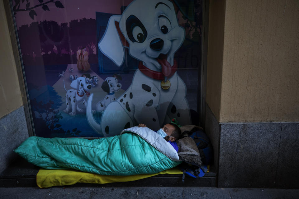 A homeless man wearing a mask sleeps in the doorway of a building, in Barcelona, Spain, Sunday, March 15, 2020. Spain's government announced Saturday that it is placing tight restrictions on movements and closing restaurants and other establishments in the nation of 46 million people as part of a two-week state of emergency to fight the sharp rise in coronavirus infections. For most people, the new coronavirus causes only mild or moderate symptoms. For some, it can cause more severe illness, especially in older adults and people with existing health problems. (AP Photo/Emilio Morenatti)