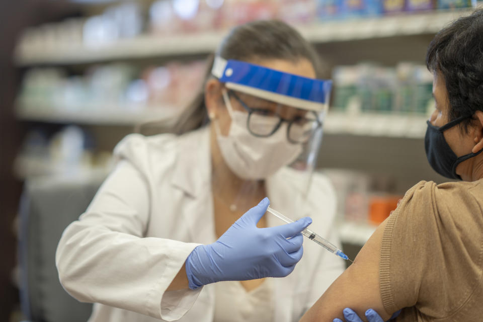 Masked senior woman getting a vaccine while at the pharmacy by a female pharmacist.