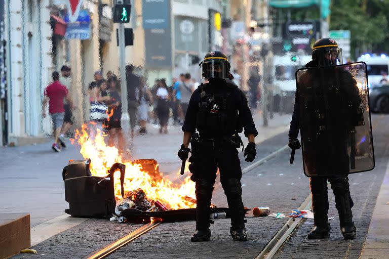 Agentes de la policía antidisturbios francesa montan guardia junto a un contenedor de basura quemado durante una manifestación contra la policía en Marsella, sur de Francia, el 1 de julio de 2023, tras una cuarta noche consecutiva de disturbios en Francia por la muerte de un adolescente a manos de la policía.