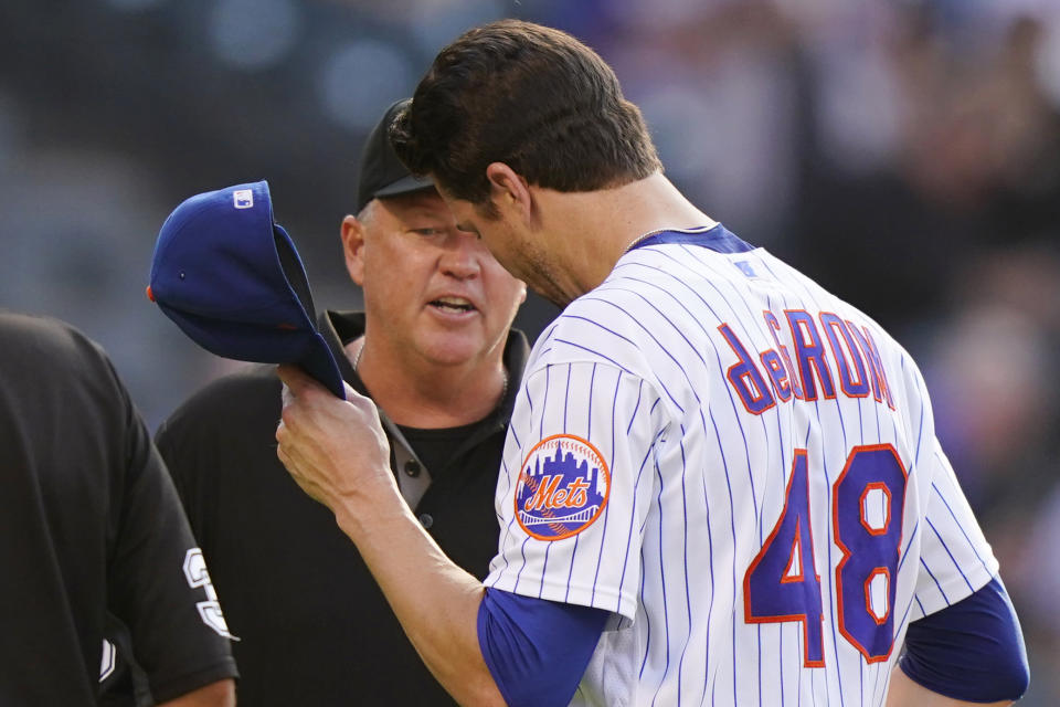 Third base umpire Ron Kulpa, left, looks inside the cap of New York Mets starting pitcher Jacob deGrom (48) after deGrom pitched in the top of the fifth inning of a baseball game against the Atlanta Braves, Monday, June 21, 2021, in New York. (AP Photo/Kathy Willens)