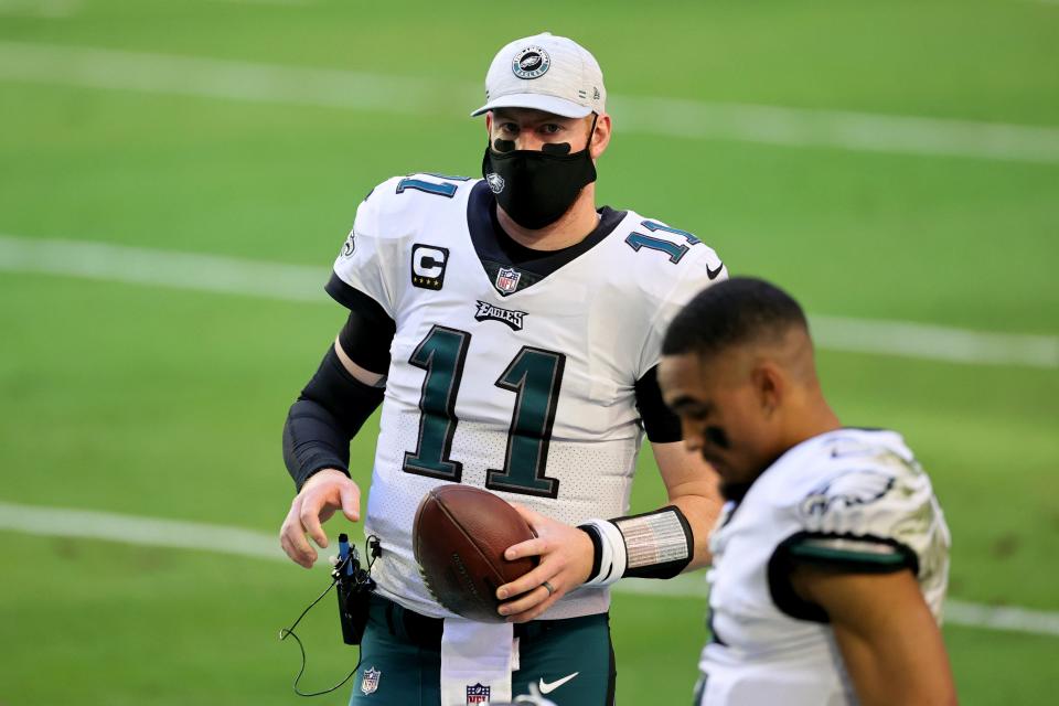 Philadelphia Eagles quarterback Carson Wentz (11) watches from the sidelines as quarterback Jalen Hurts (foreground) starts in his place during a game against the Arizona Cardinals on Dec. 20, 2020, in Glendale, Ariz.