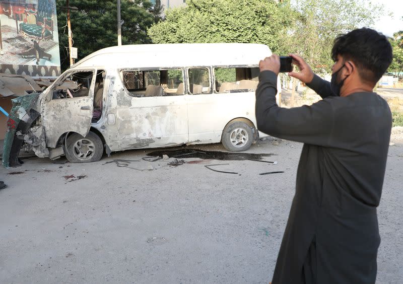 An Afghan man takes pictures of a bus which was carrying employees of an Afghan television station and was bombed, in Kabul