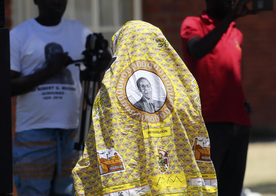 A man covers himself with a cloth bearing the portrait of former Zimbabwean President Robert Mugabe at his rural home in Zvimba, about 100 kilometer north west of the capital Harare, Saturday, Sept. 28, 2019. According to a family spokesperson Mugabe is expected to be buried at the residence after weeks of drama mystery and contention over his burial place.(AP Photo/Tsvangirayi Mukwazhi)