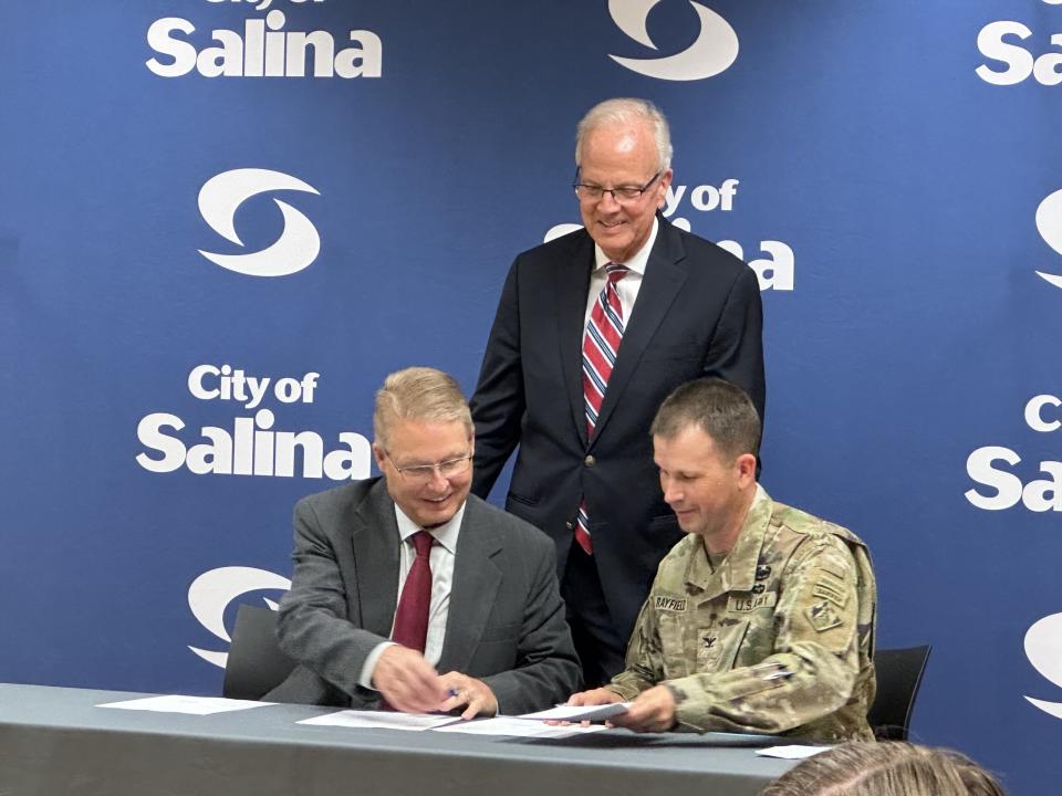 U.S. Sen. Jerry Moran stands over Salina Mayor Bill Longbine and U.S. Army Corps of Engineers Col. Travis Rayfield as Rayfield and Longbine sign a cost-share agreement, indicating the first step toward a project to bring flowing water back to the downtown portion of the Smoky Hill River. 