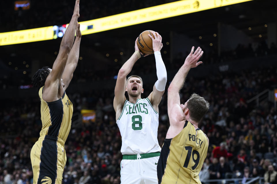 Boston Celtics center Kristaps Porzingis (8) shoots while defended by Toronto Raptors center Jakob Poeltl (19) and forward Scottie Barnes (4) during the second half of an NBA basketball game in Toronto on Friday, Nov. 17, 2023. (Christopher Katsarov/The Canadian Press via AP)