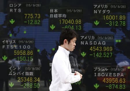 A passerby walks past an electric screen displaying stock market indices of various countries outside at a brokerage in Tokyo, Japan, September 29, 2015. REUTERS/Issei Kato