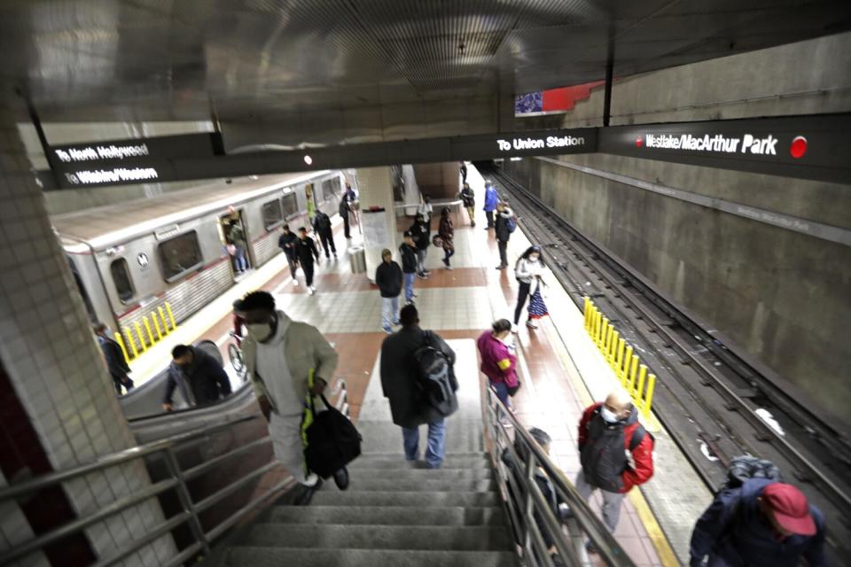 People walk down stairs to a subway platform with a train on one side.