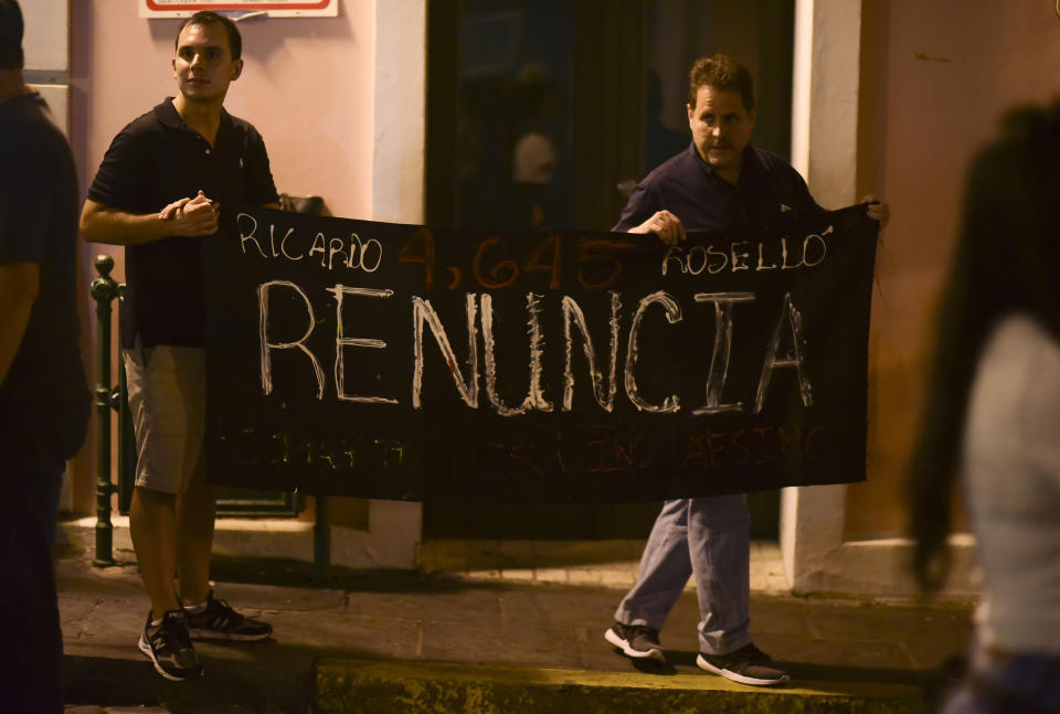 Citizens carrying a banner that reads in Spanish "Ricarod Rosello, renounce" protest near the executive mansion denouncing a wave of arrests for corruption that has shaken the country and demanding the resignation of Gov. Ricardo Rosello, in San Juan, Puerto Rico, Thursday, July 11, 2019. Puerto Rico's former secretary of education and 5 other people have been arrested on charges of steering federal money to unqualified, politically connected contractors. U.S. Attorney for Puerto Rico Rosa Emilia Rodríguez said Gov. Rossello was not involved in the investigation. (AP Photo/Carlos Giusti)