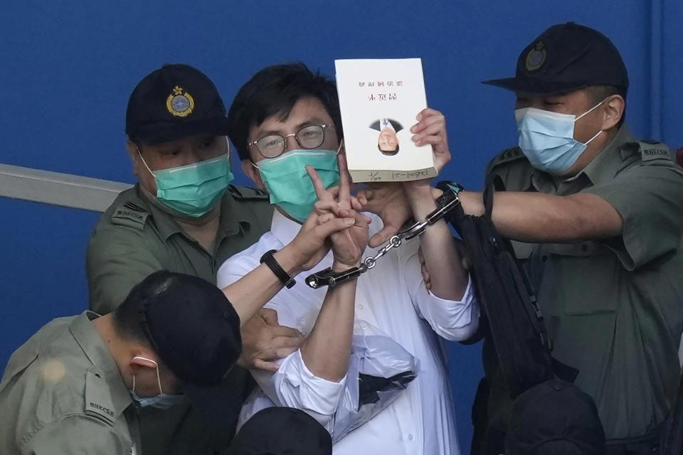 Pro-democracy activist Avery Ng, center, holds a book with a cover picture of Chinese President Xi Jinping as he is escorted by Correctional Services officers to a prison van for a court in Hong Kong, Friday, May 28, 2021. Jimmy Lai and nine others, including Ng, accused of "incitement to knowingly take part in an unauthorized assembly" on Oct. 1, 2019, were sentencing in court. Lai is already serving a 14-month sentence for his role in two other unauthorized assemblies during a period when Hong Kong residents were involved in mass anti-government protests. (AP Photo/Kin Cheung)