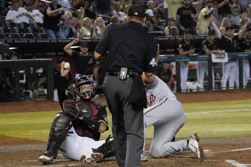 Arizona Diamondbacks catcher Jose Herrera, left, shows the ball to home plate umpire Robert Ortiz, center, after tagging out Washington Nationals' Dominic Smith, right, in the second inning during a baseball game, Sunday, May 7, 2023, in Phoenix. (AP Photo/Darryl Webb)