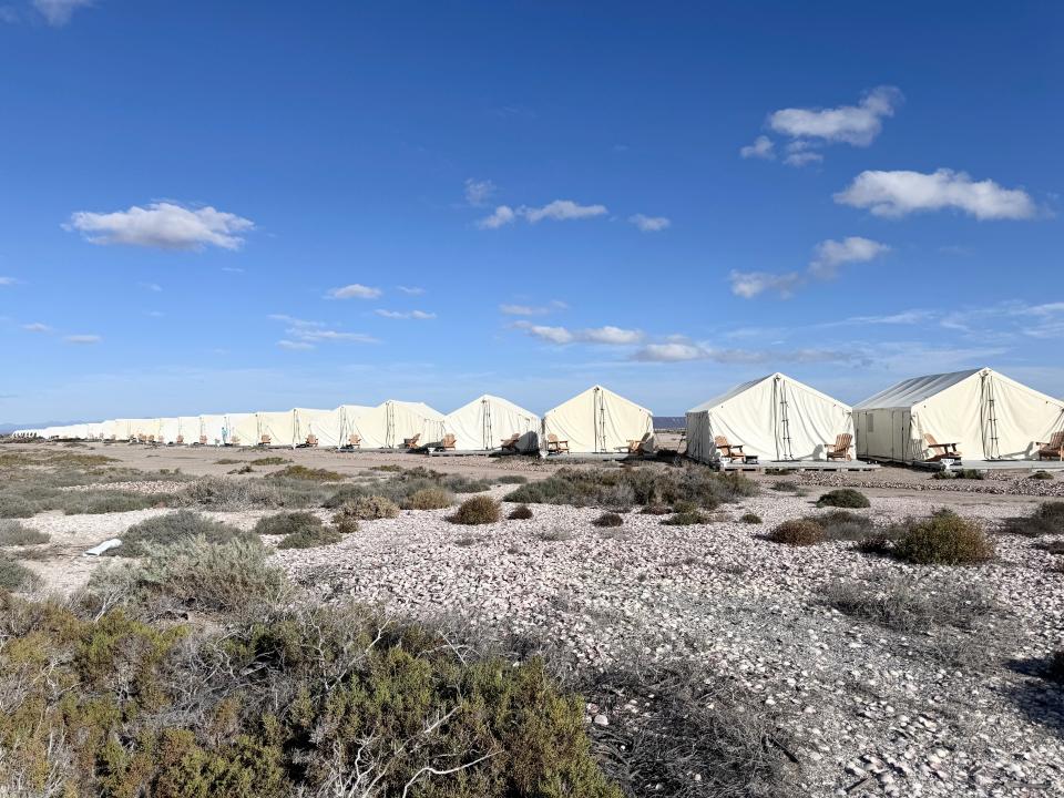 A series of white tents with Adirondack chairs outside in a remote area.