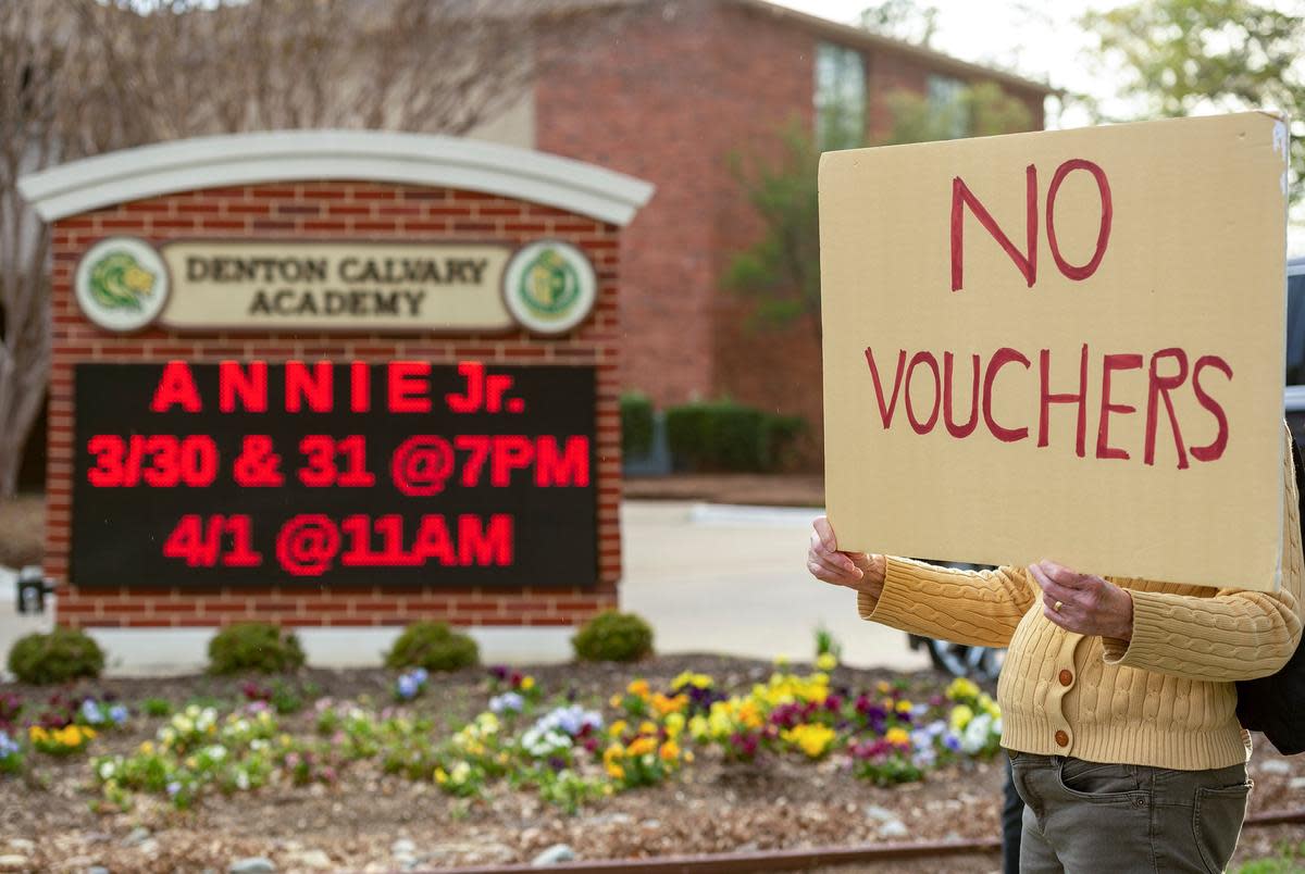 A woman holds a sign reading "No Vouchers" outside Denton Calvary Academy on March 27, 2023.
