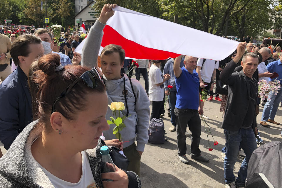 People hold an old Belarusian National flag and gather at the place where Alexander Taraikovsky died amid the clashes protesting the election results, during his civil funeral in Minsk, Belarus, Saturday, Aug. 15, 2020. During the four nights that followed, black-clad riot police detained thousands of largely peaceful demonstrators in Minsk and other cities after firing tear gas, rubber bullets and stun grenades. (AP Photo/Sergei Grits)