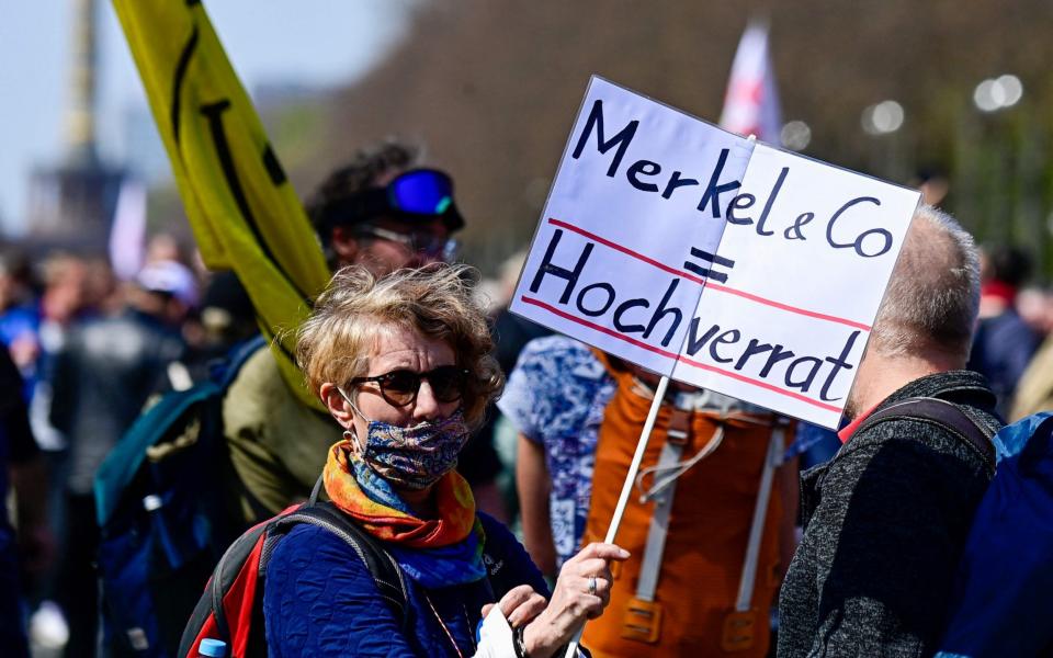 An anti Covid-19 protestor holds a placard reading, " Merkel & CO = High treason) while taking part in a demonstration in Berlin - TOBIAS SCHWARZ /  AFP