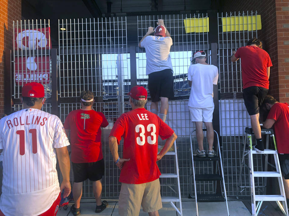 Phandemic Krew members look through a gate during a baseball game between the Philadelphia Phillies and Atlanta Braves in Philadelphia, Monday, Aug. 10, 2020. (AP Photo/Dan Gelston)